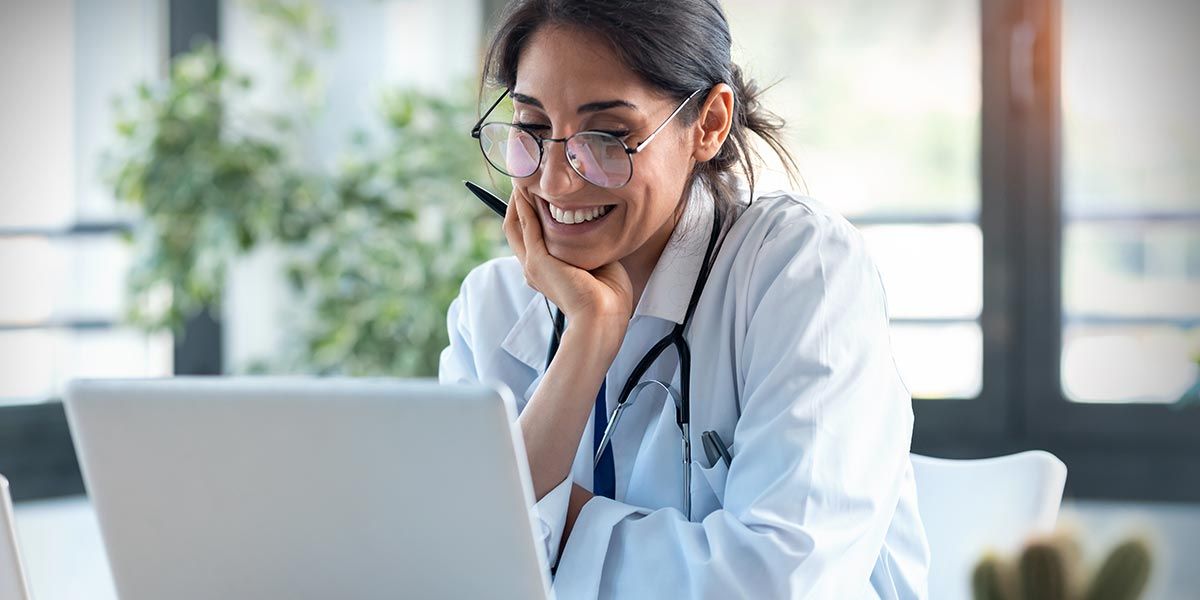 A doctor smiling while working on a laptop.